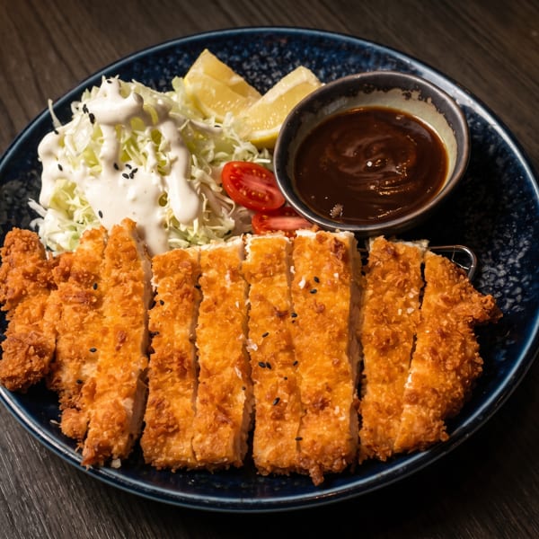 Crispy fried chicken cutlets, shredded cabbage salad with dressing, lemon wedges, and dipping sauce.