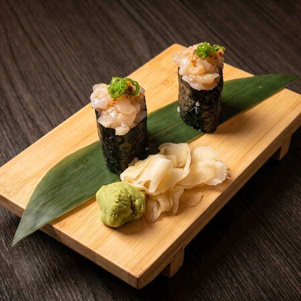 Two gunkan maki sushi with scallops and green onions, served with wasabi and pickled ginger.