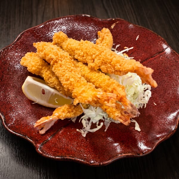 Crispy fried shrimp tempura with shredded cabbage and a lemon wedge on a red plate.