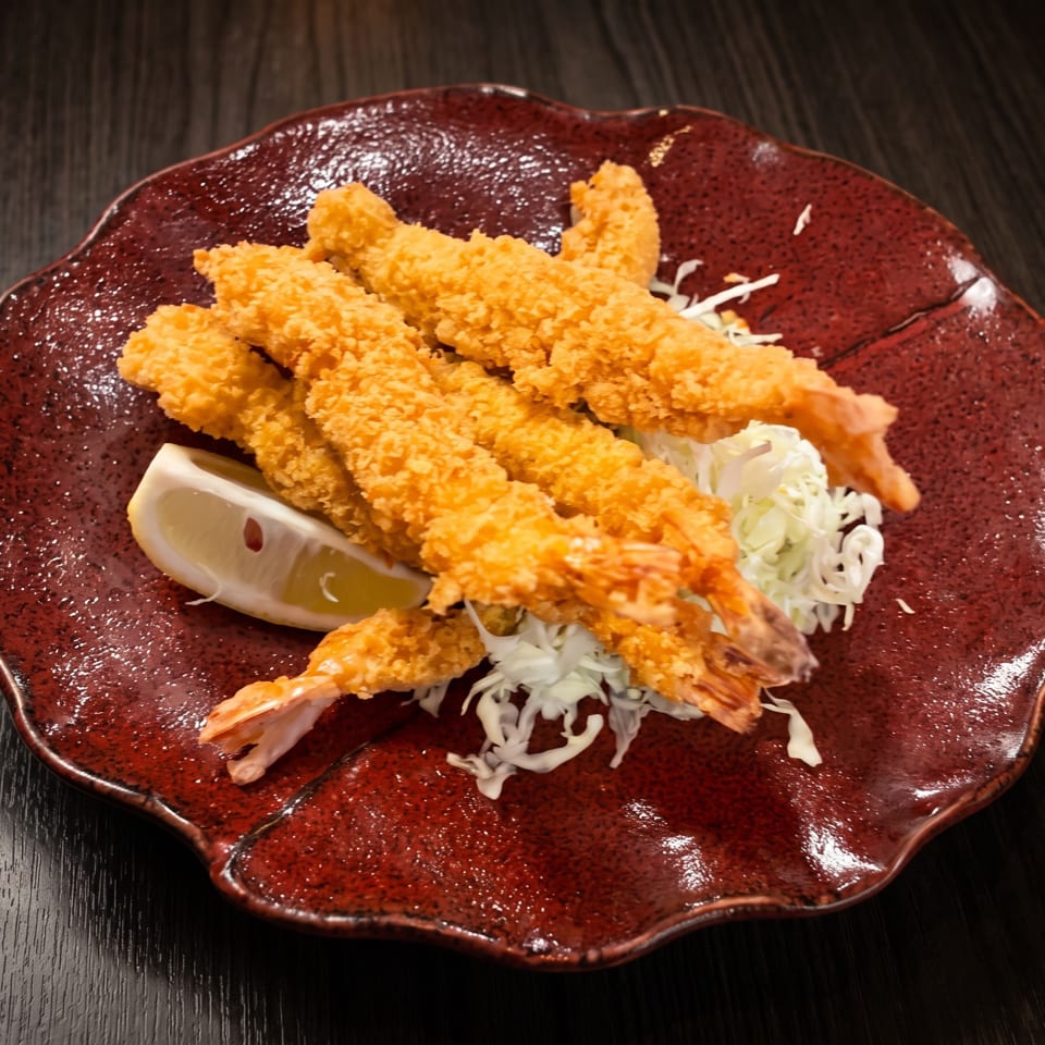 Crispy fried shrimp tempura with shredded cabbage and a lemon wedge on a red plate.
