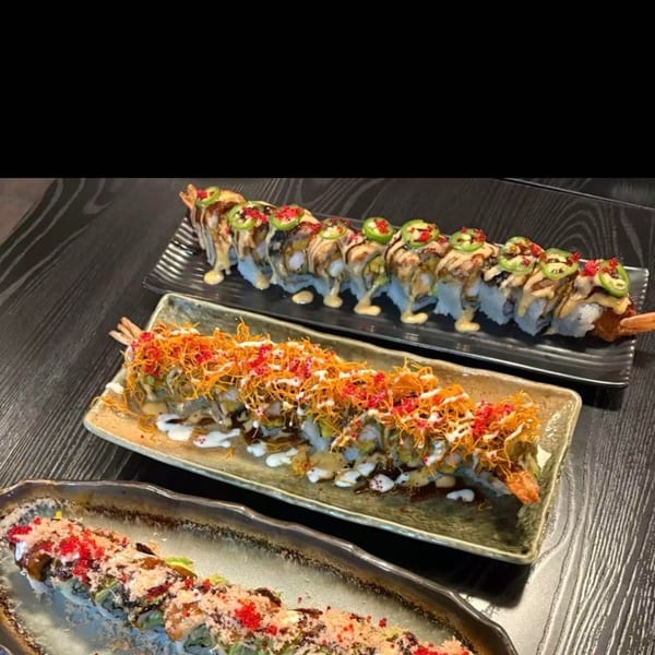 Three long plates of sushi rolls, each with unique toppings and sauces, on a dark wooden table.