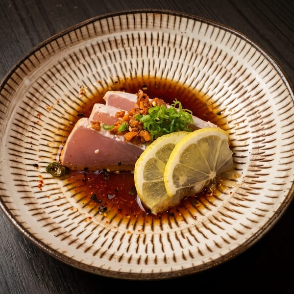Seared tuna sashimi with lemon slices, green onions, and crispy garlic in a dark sauce.